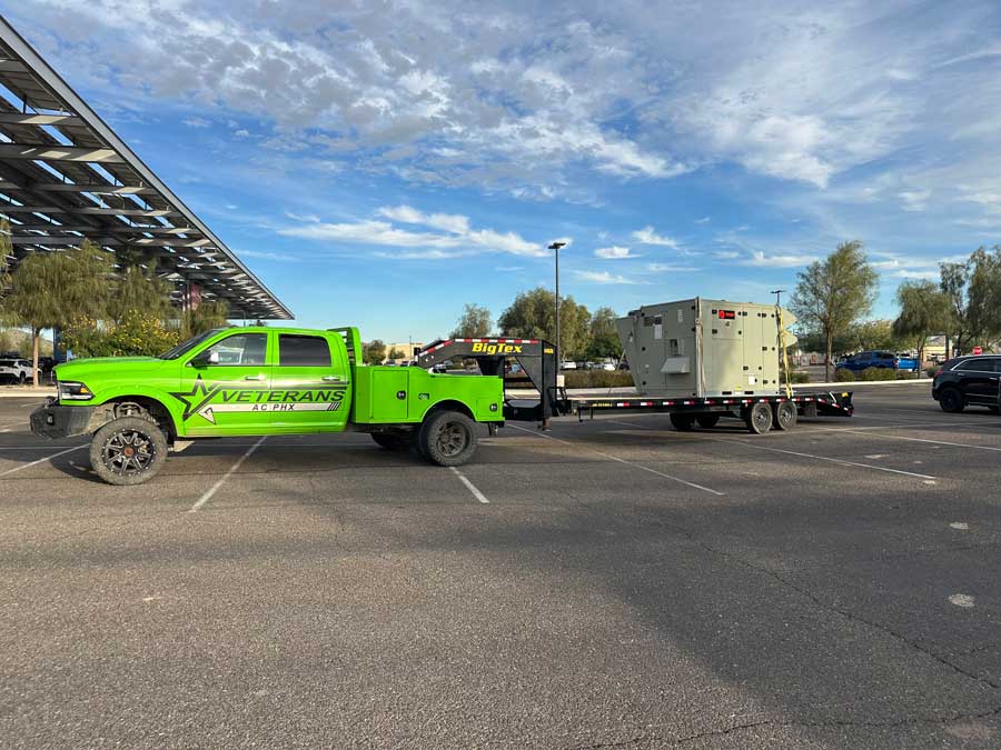 Veterans AC PHX truck towing a large HVAC unit on a BigTex trailer