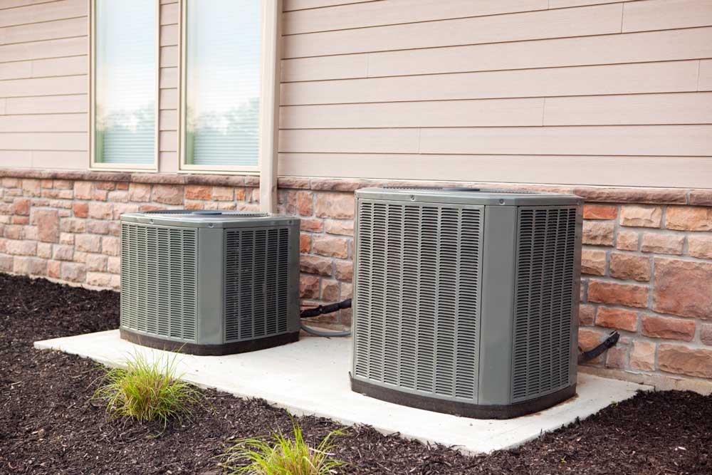 Two outdoor AC units installed beside a house