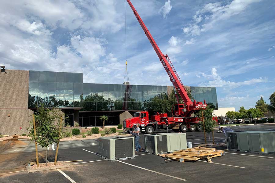 Crane lifting HVAC unit onto a commercial building rooftop