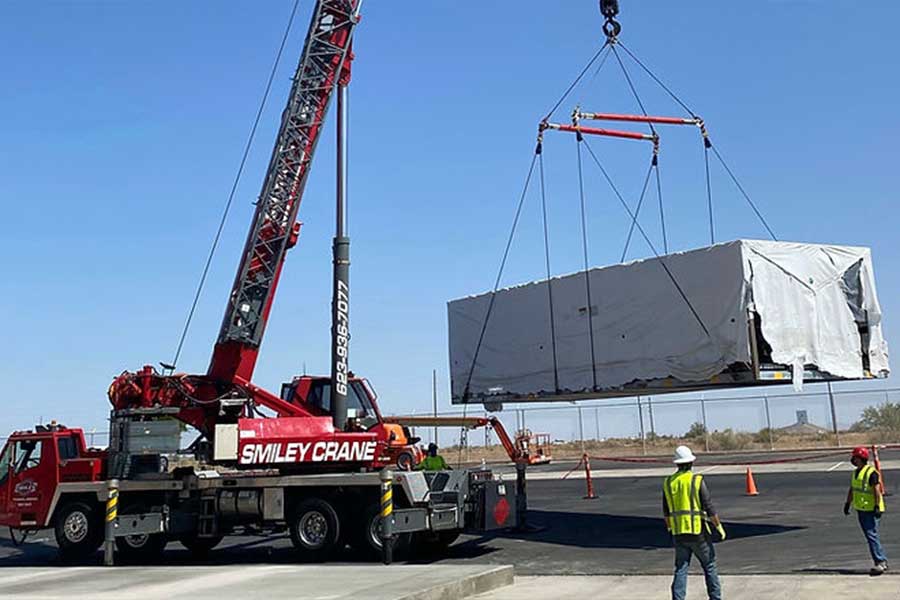 Crane lifting a large wrapped HVAC unit as workers guide the operation