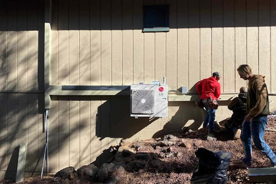 Technicians installing an LG mini-split system on the exterior wall of a house